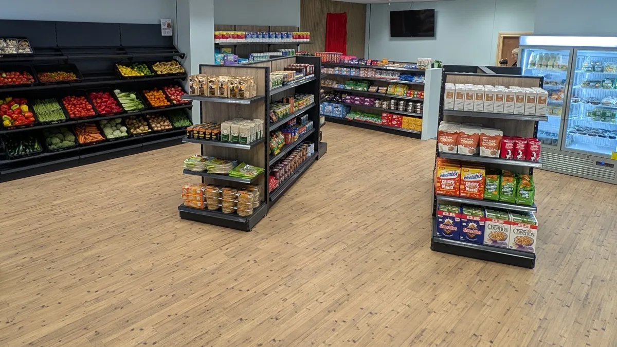 Inside the SEK Community Food Shop in Chatham: crates of fresh fruit and vegetables along the left wall, shelves of packaged food and breakfast cereals, and a chiller cabinet on the right.